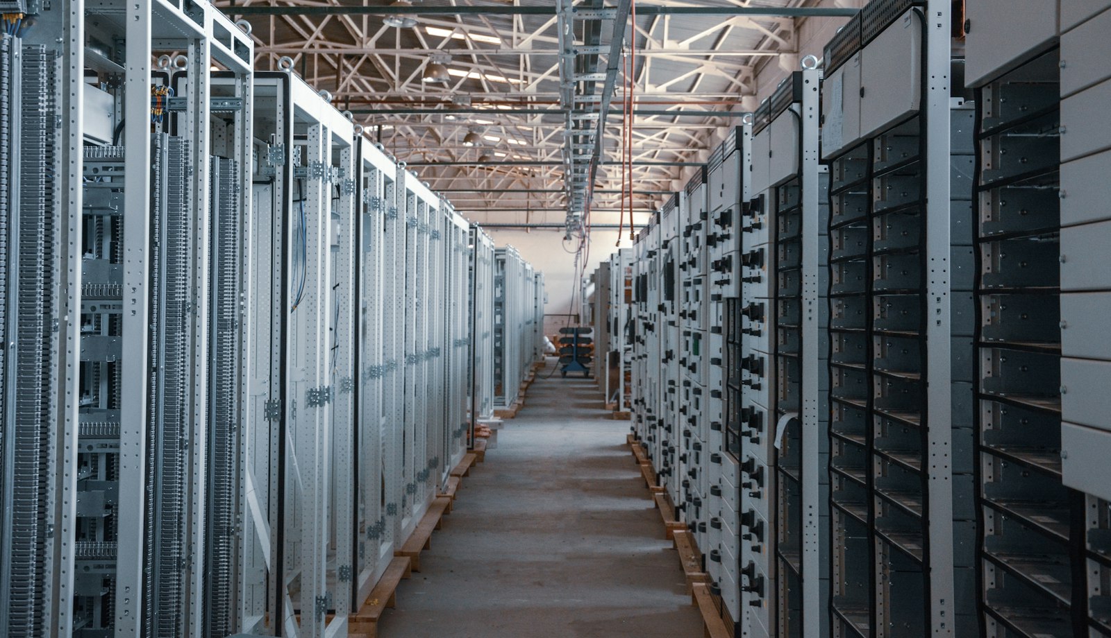 A long aisle of new equipment cabinets standing on pallets in a hall that is being fitted out